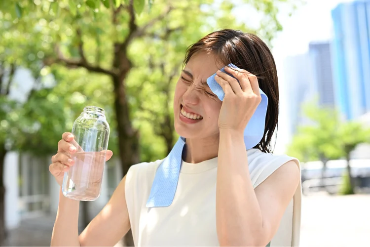 Woman outdoors in Singapore humidity wiping sweat away while experiencing heat rash symptoms.